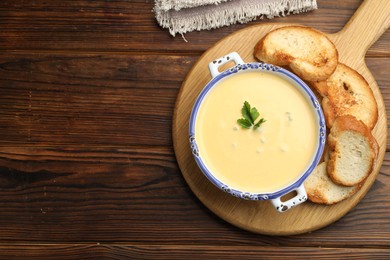Photo of Tasty cheese dipping sauce in bowl and croutons on wooden table, top view. Space for text