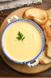Photo of Tasty cheese dipping sauce in bowl and croutons on wooden table, top view