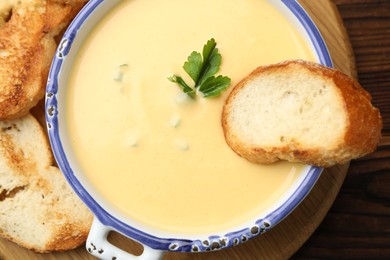 Photo of Tasty cheese dipping sauce in bowl and croutons on wooden table, top view