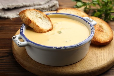 Photo of Tasty cheese dipping sauce in bowl and croutons on wooden table, closeup