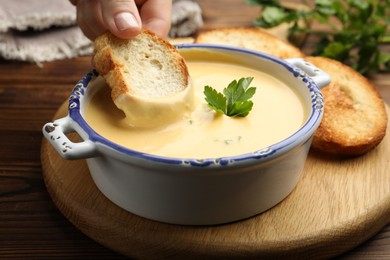 Photo of Woman dipping crouton into tasty cheese sauce at wooden table, closeup