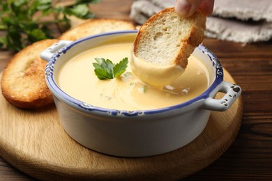 Photo of Woman dipping crouton into tasty cheese sauce at wooden table, closeup