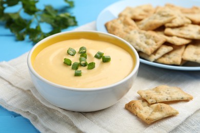 Photo of Tasty cheese dipping sauce in bowl and crackers on light blue table, closeup