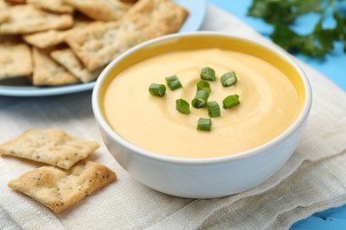 Photo of Tasty cheese dipping sauce in bowl and crackers on table, closeup