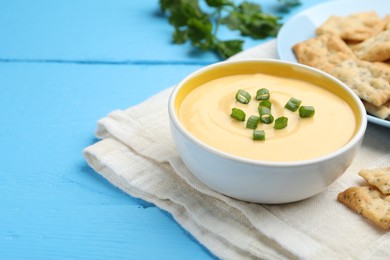 Photo of Tasty cheese dipping sauce in bowl and crackers on light blue wooden table, closeup. Space for text