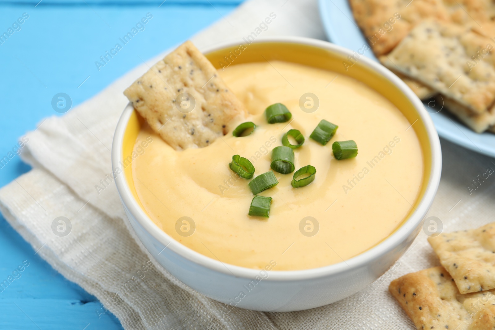 Tasty cheese dipping sauce in bowl and crackers on light blue wooden table, closeup Photo of Tasty cheese dipping sauce in bowl and crackers on light blue wooden table, closeup