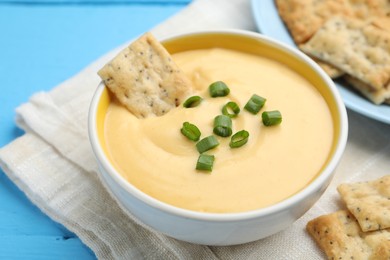 Photo of Tasty cheese dipping sauce in bowl and crackers on light blue wooden table, closeup
