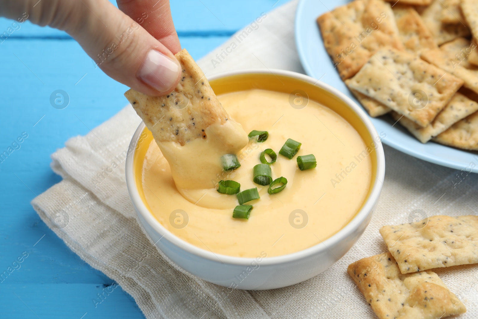 Woman dipping cracker into tasty cheese sauce at light blue wooden table, closeup Photo of Woman dipping cracker into tasty cheese sauce at light blue wooden table, closeup