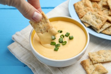 Photo of Woman dipping cracker into tasty cheese sauce at light blue wooden table, closeup