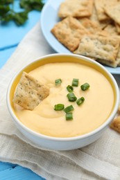 Photo of Tasty cheese dipping sauce in bowl and crackers on table, closeup
