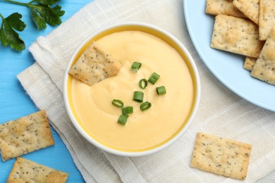 Photo of Tasty cheese dipping sauce in bowl and crackers on light blue wooden table, flat lay