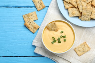 Photo of Tasty cheese dipping sauce in bowl and crackers on light blue wooden table, flat lay. Space for text