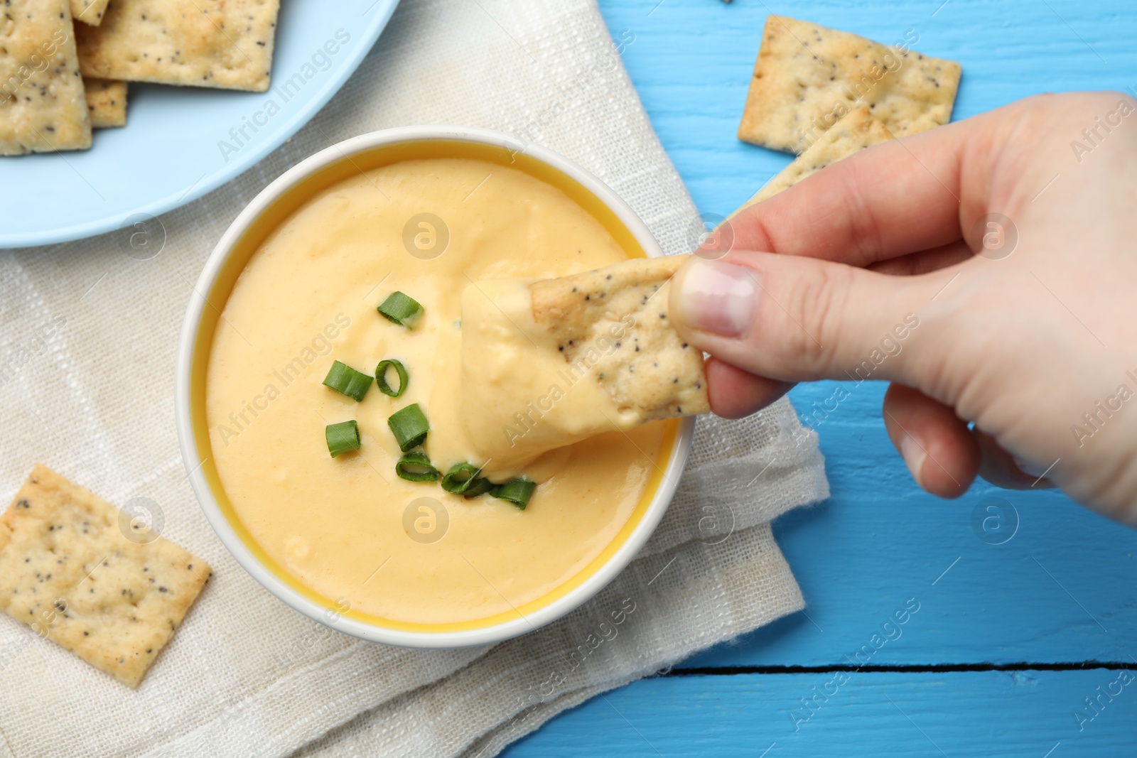 Woman dipping cracker into tasty cheese sauce at light blue wooden table, top view Photo of Woman dipping cracker into tasty cheese sauce at light blue wooden table, top view