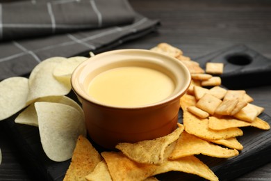 Photo of Tasty cheese dipping sauce in bowl and different snacks on table, closeup