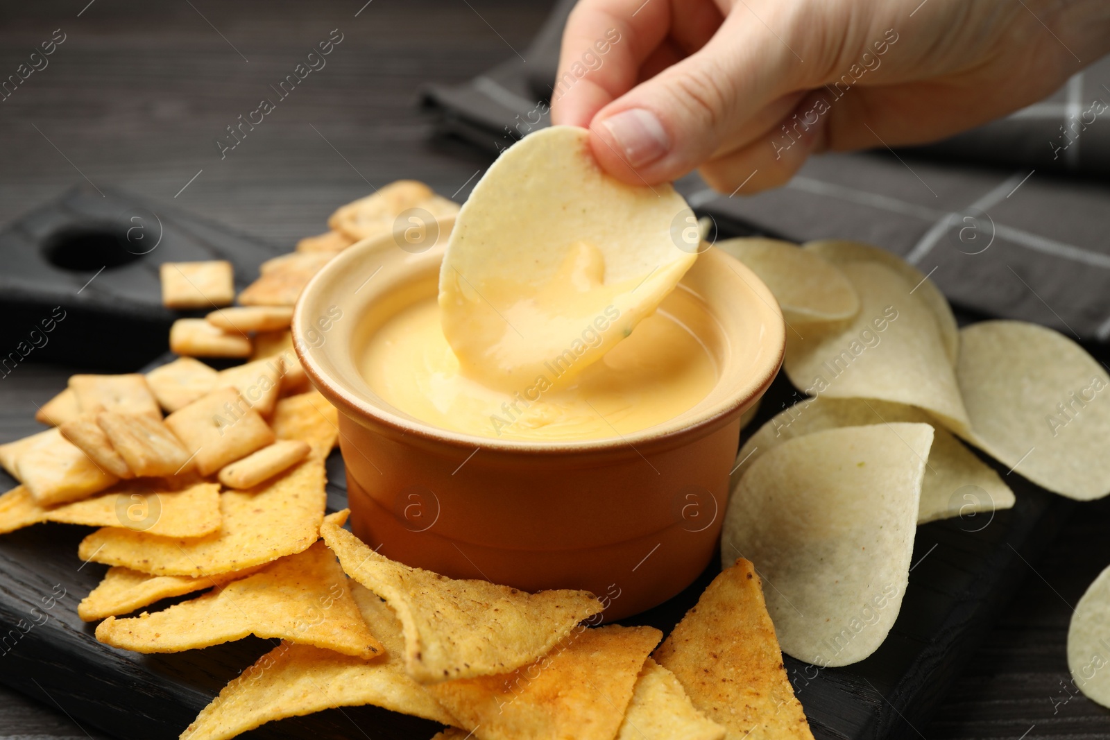 Photo of Woman dipping potato chip into tasty cheese sauce at table, closeup
