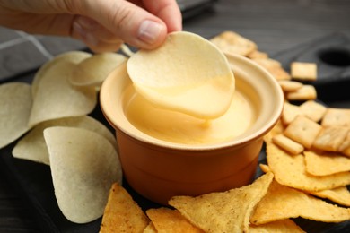 Photo of Woman dipping potato chip into tasty cheese sauce at table, closeup