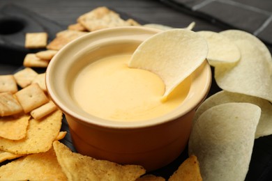 Photo of Tasty cheese dipping sauce in bowl and different snacks on table, closeup