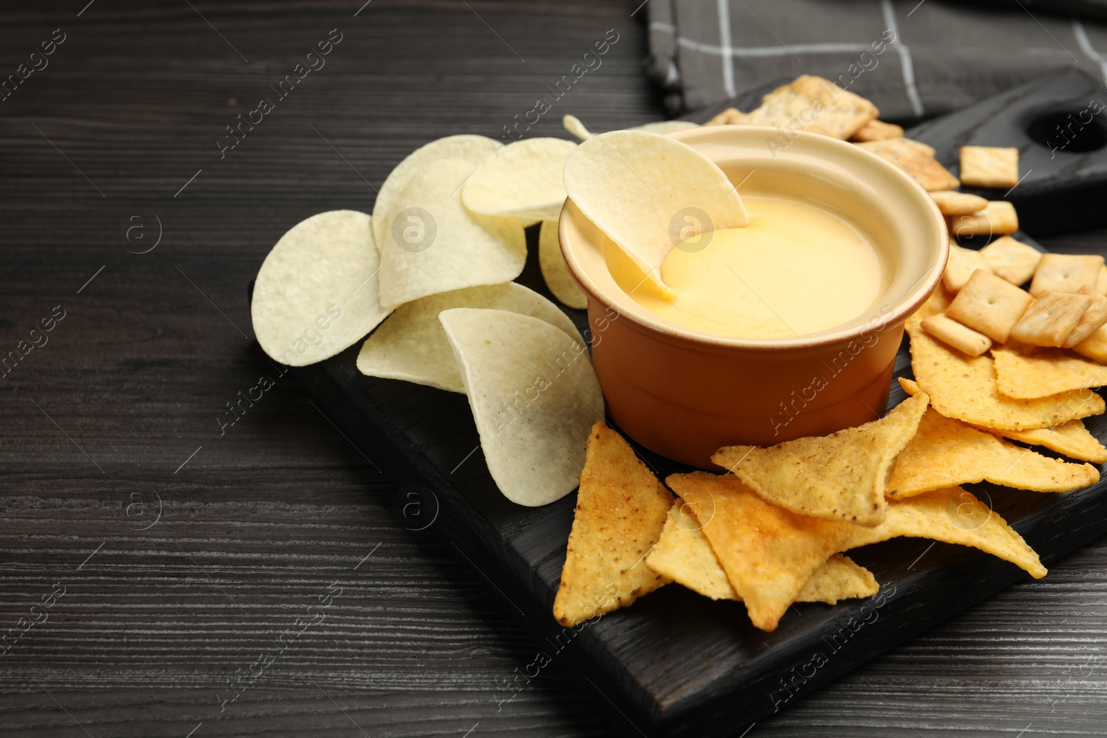 Tasty cheese dipping sauce in bowl and different snacks on dark wooden table, closeup. Space for text Photo of Tasty cheese dipping sauce in bowl and different snacks on dark wooden table, closeup. Space for text
