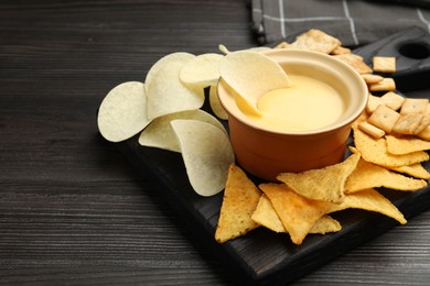 Photo of Tasty cheese dipping sauce in bowl and different snacks on dark wooden table, closeup. Space for text