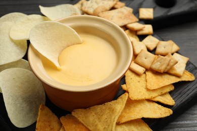 Photo of Tasty cheese dipping sauce in bowl and different snacks on table, closeup