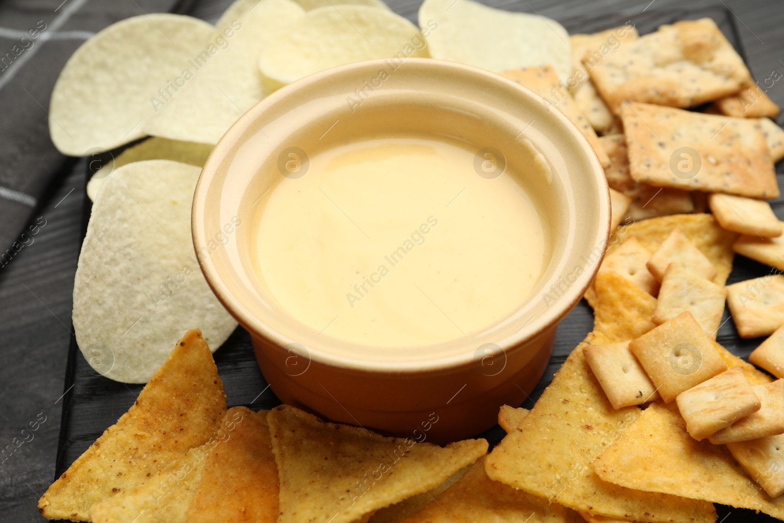 Tasty cheese dipping sauce in bowl and different snacks on table, closeup Photo of Tasty cheese dipping sauce in bowl and different snacks on table, closeup
