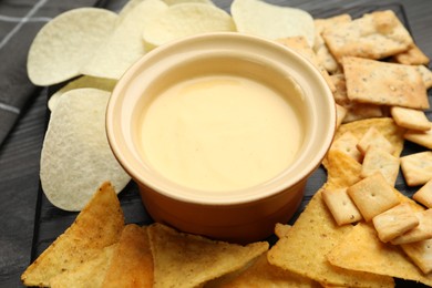 Photo of Tasty cheese dipping sauce in bowl and different snacks on table, closeup