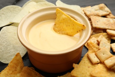 Photo of Tasty cheese dipping sauce in bowl and different snacks on table, closeup
