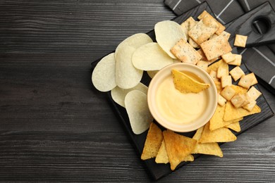 Photo of Tasty cheese dipping sauce in bowl and different snacks on dark wooden table, top view. Space for text