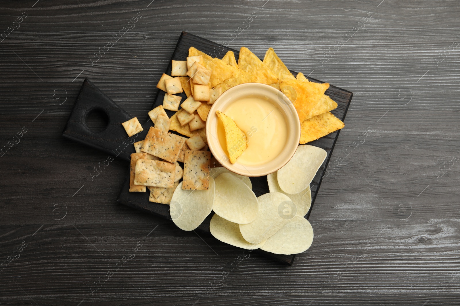 Tasty cheese dipping sauce in bowl and different snacks on dark wooden table, top view Photo of Tasty cheese dipping sauce in bowl and different snacks on dark wooden table, top view