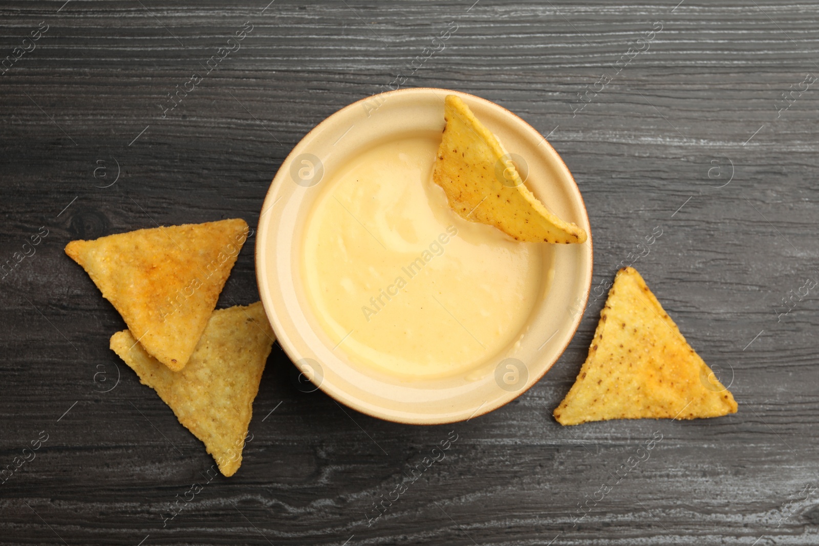 Tasty cheese dipping sauce in bowl and nacho chips on dark wooden table, flat lay Photo of Tasty cheese dipping sauce in bowl and nacho chips on dark wooden table, flat lay