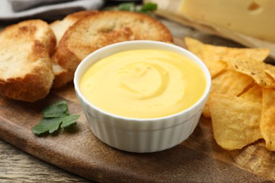 Photo of Tasty cheese dipping sauce in bowl and snacks on table, closeup
