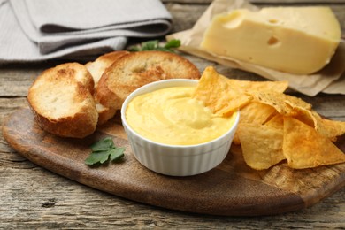 Photo of Tasty cheese dipping sauce in bowl, nacho chips and croutons on wooden table, closeup