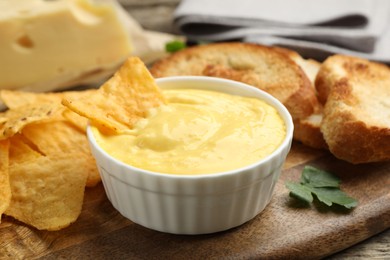 Photo of Tasty cheese dipping sauce in bowl, nacho chips and croutons on table, closeup