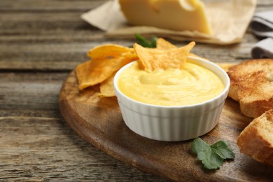 Photo of Tasty cheese dipping sauce in bowl, nacho chips and croutons on wooden table, closeup