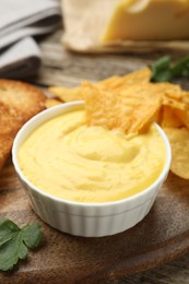 Photo of Tasty cheese dipping sauce in bowl and nacho chips on table, closeup