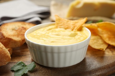 Photo of Tasty cheese dipping sauce in bowl, nacho chips and croutons on table, closeup