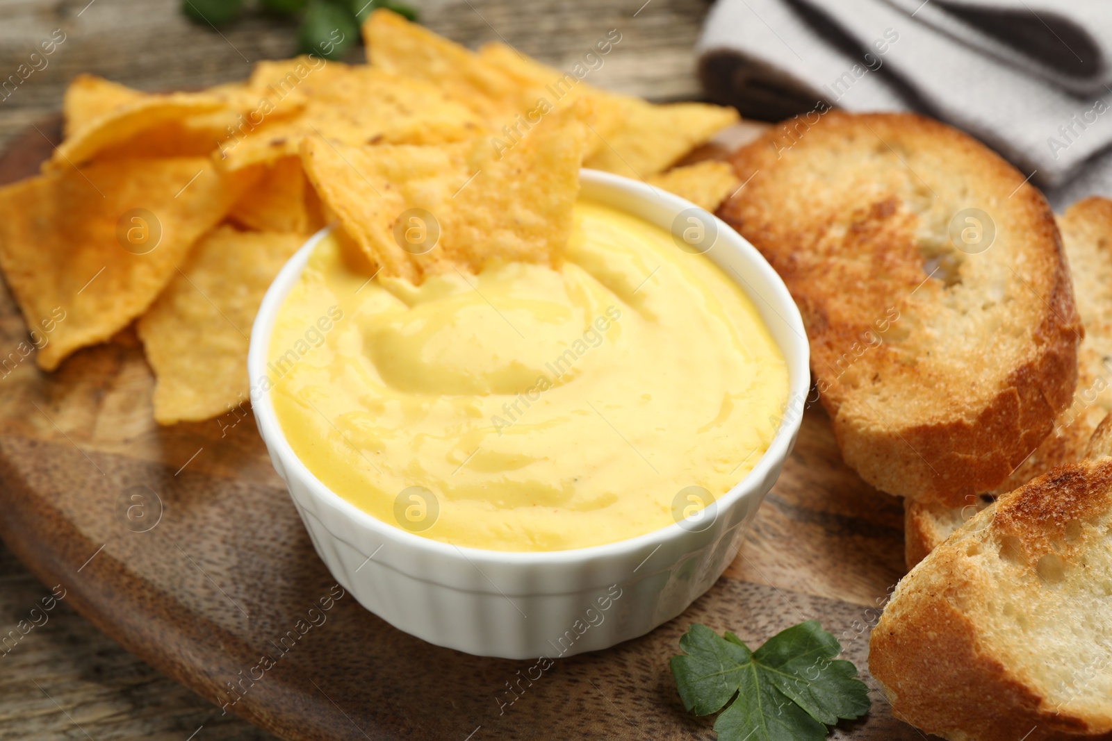 Tasty cheese dipping sauce in bowl, nacho chips and croutons on table, closeup Photo of Tasty cheese dipping sauce in bowl, nacho chips and croutons on table, closeup