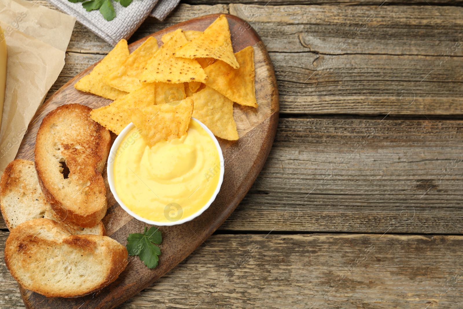 Tasty cheese dipping sauce in bowl, nacho chips and croutons on wooden table, top view. Space for text Photo of Tasty cheese dipping sauce in bowl, nacho chips and croutons on wooden table, top view. Space for text