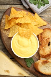 Photo of Tasty cheese dipping sauce in bowl, nacho chips and croutons on wooden table, flat lay