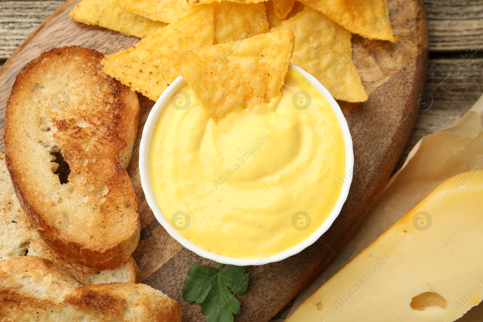 Tasty cheese dipping sauce in bowl, nacho chips and croutons on wooden table, flat lay Photo of Tasty cheese dipping sauce in bowl, nacho chips and croutons on wooden table, flat lay