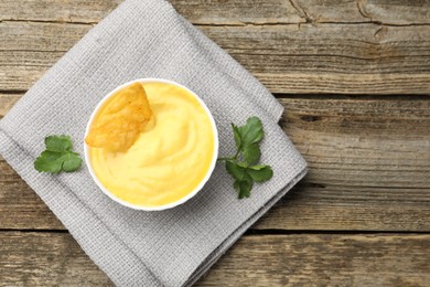 Photo of Tasty dipping cheese sauce in bowl, nacho chip and parsley on wooden table, top view. Space for text