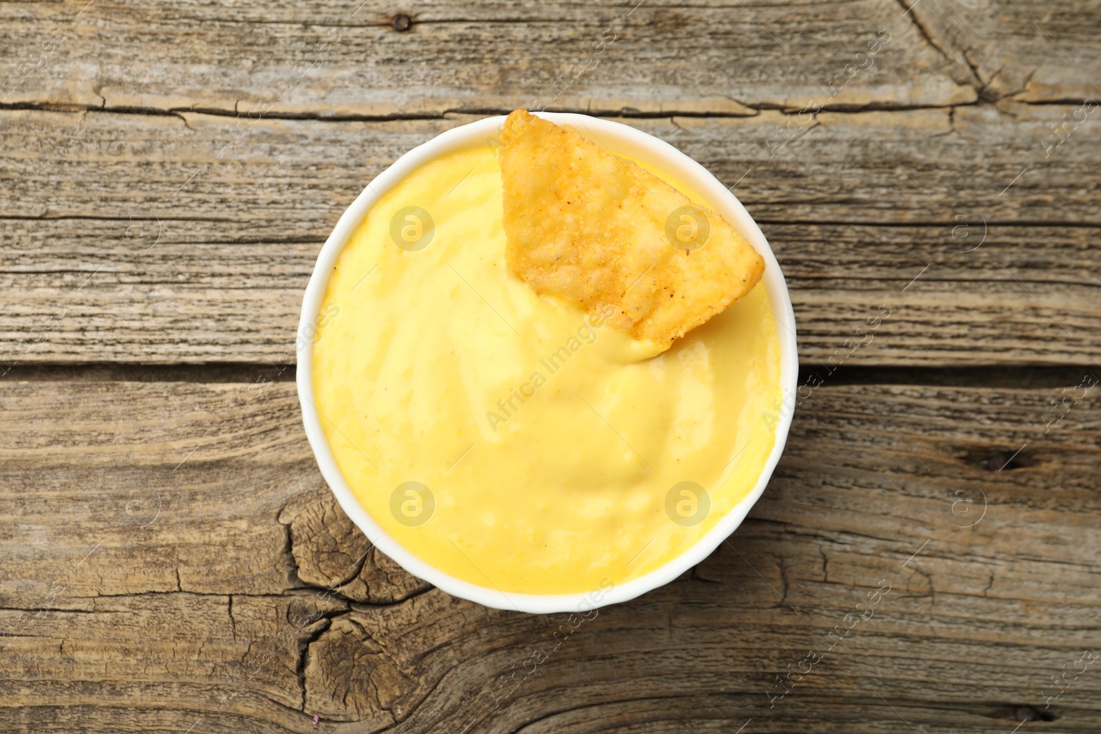 Tasty dipping cheese sauce in bowl and nacho chip on wooden table, top view Photo of Tasty dipping cheese sauce in bowl and nacho chip on wooden table, top view