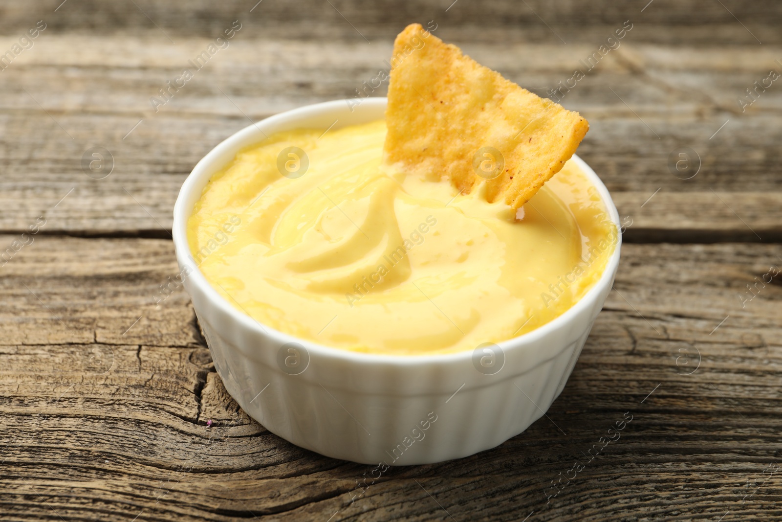 Tasty dipping cheese sauce in bowl and nacho chip on wooden table, closeup Photo of Tasty dipping cheese sauce in bowl and nacho chip on wooden table, closeup