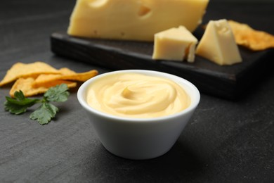Photo of Tasty dipping cheese sauce in bowl, nacho chips and parsley on black table, closeup