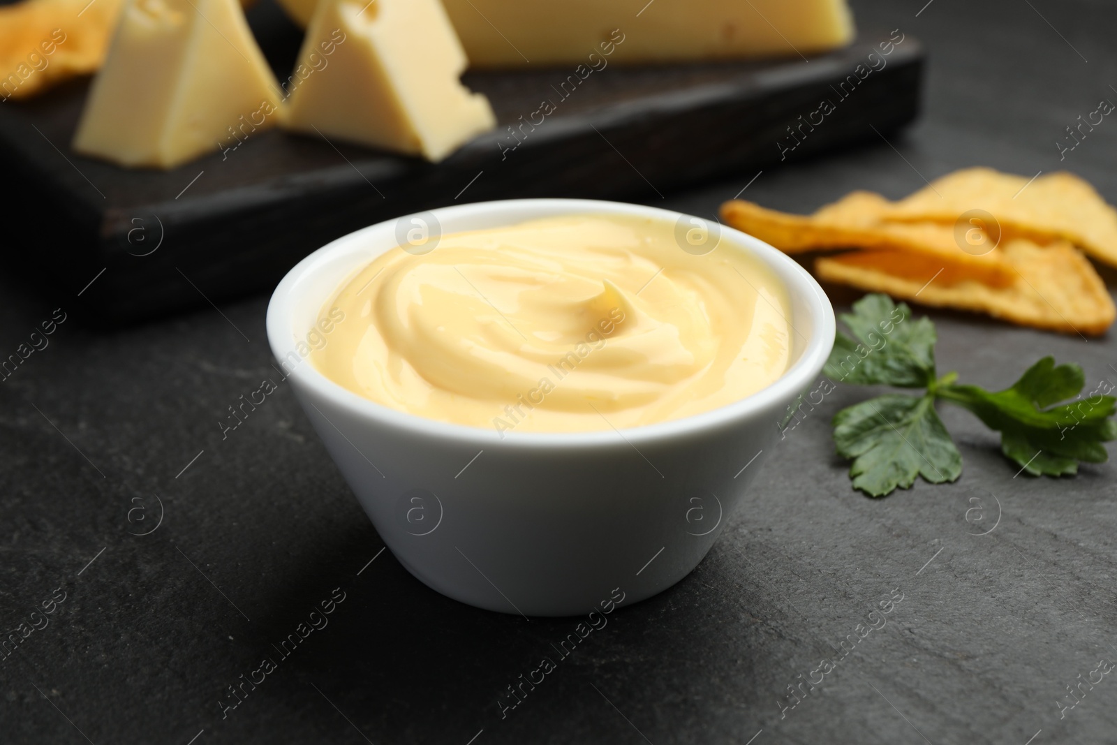 Tasty dipping cheese sauce in bowl, nacho chips and parsley on black table, closeup Photo of Tasty dipping cheese sauce in bowl, nacho chips and parsley on black table, closeup