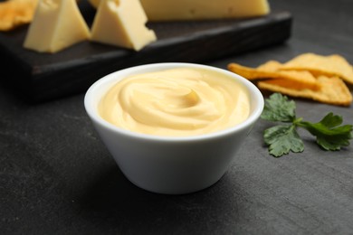 Photo of Tasty dipping cheese sauce in bowl, nacho chips and parsley on black table, closeup