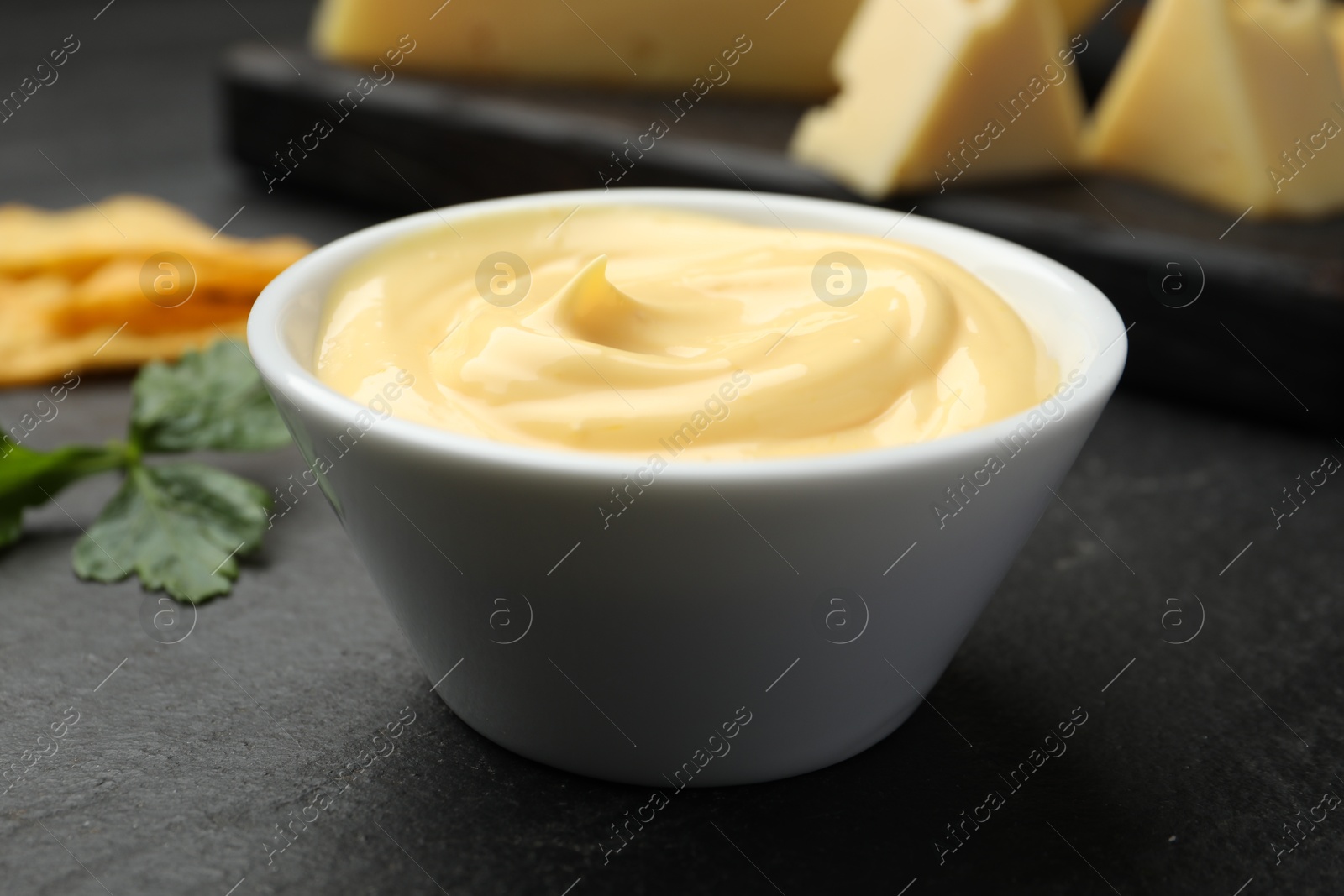 Photo of Tasty dipping cheese sauce in bowl, nacho chips and parsley on black table, closeup