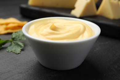 Photo of Tasty dipping cheese sauce in bowl, nacho chips and parsley on black table, closeup