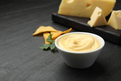 Photo of Tasty dipping cheese sauce in bowl, nacho chips and parsley on black table, closeup. Space for text