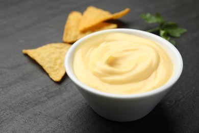 Photo of Tasty dipping cheese sauce in bowl, nacho chips and parsley on black table, closeup. Space for text